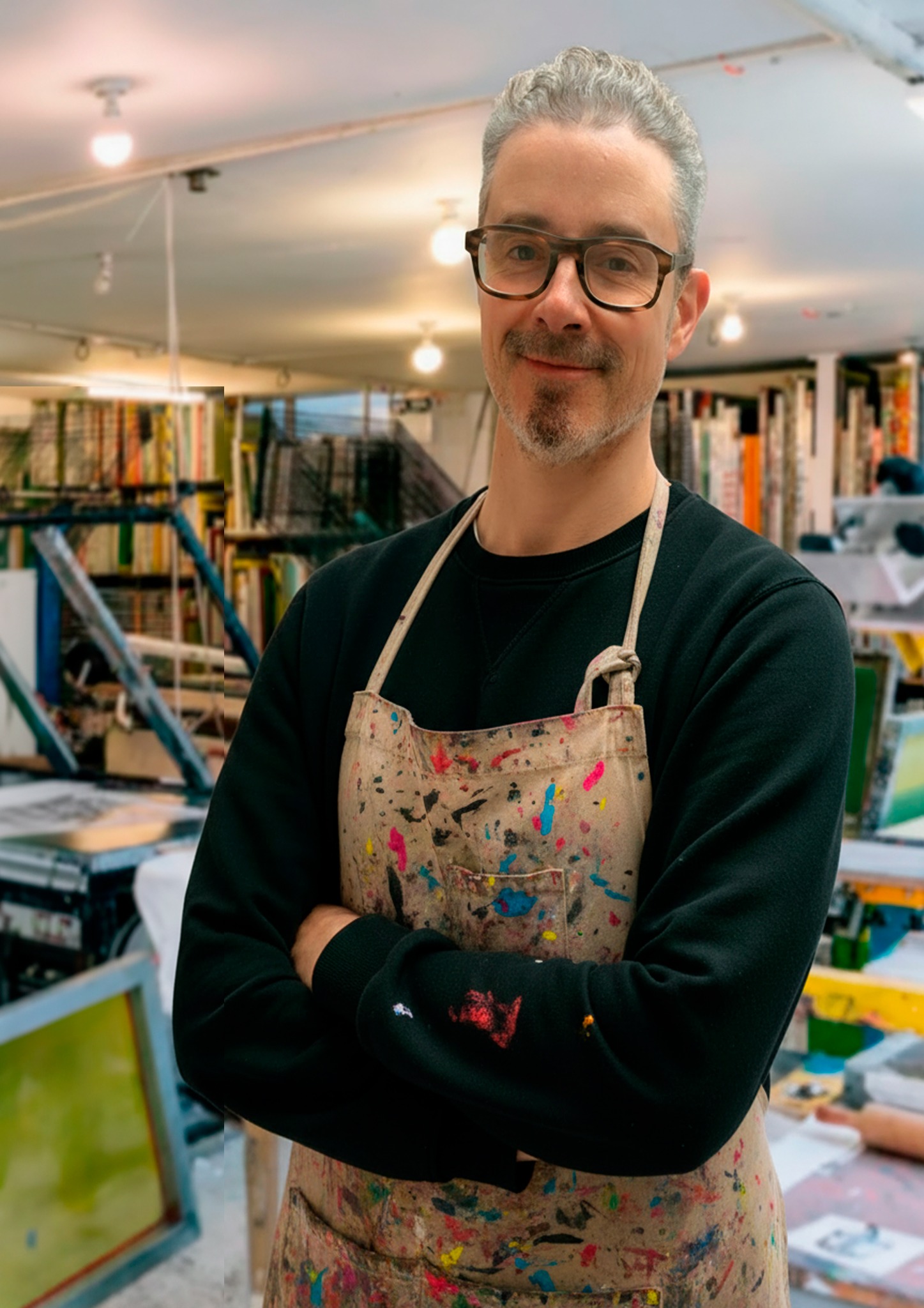 Gerard McDonagh at Print Club Gerard McDonagh standing with arms folded in a paint-marked apron at Print Club, with printing equipment behind him.
